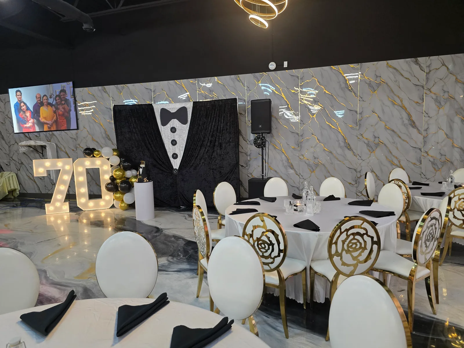 Milestone birthday setup in the Rawaayt banquet hall, Edmonton — lit marquee numbers, black-and-gold balloon garland and a themed backdrop against the marble feature wall