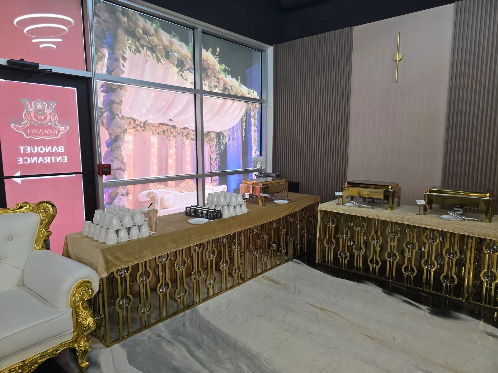 Buffet service line in the Rawaayt banquet hall, Edmonton — gold chafing dishes on skirted tables beside the banquet entrance